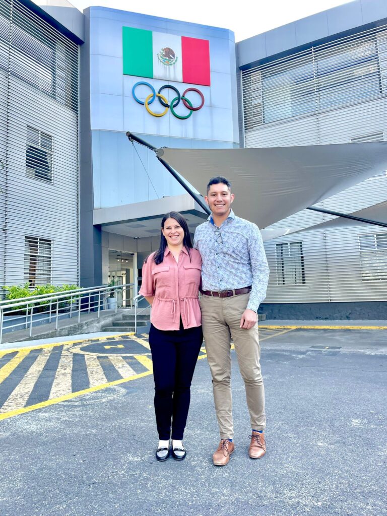 Representantes frente al edificio del Comité Olímpico Mexicano, con la bandera de México y los anillos olímpicos en la fachada, durante una visita institucional relacionada con sostenibilidad y deporte