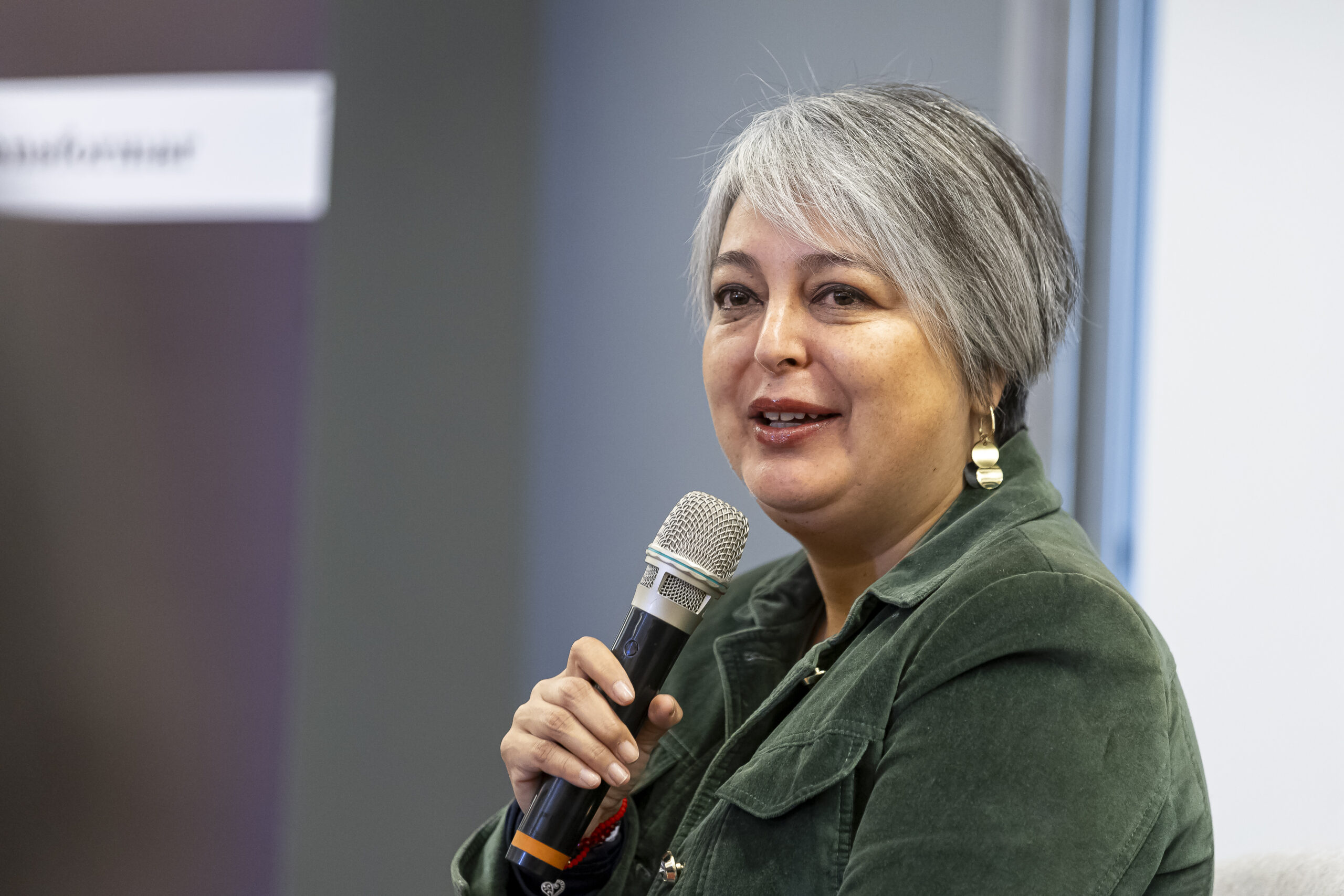 Janet Jara en una entrevista para las presidenciales 2025. Micrófono en mano, fondo gris.